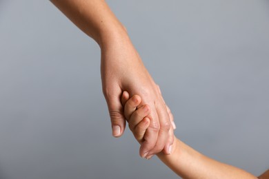 Photo of Mother and child holding hands on grey background, closeup