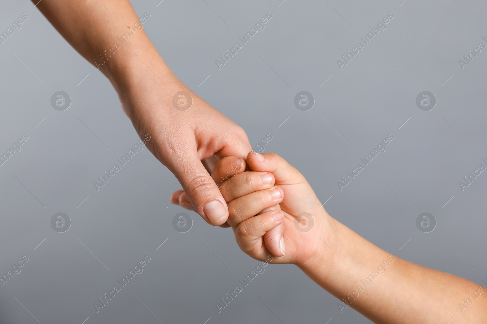 Photo of Mother and child holding hands on grey background, closeup