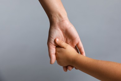 Photo of Mother and child holding hands on grey background, closeup