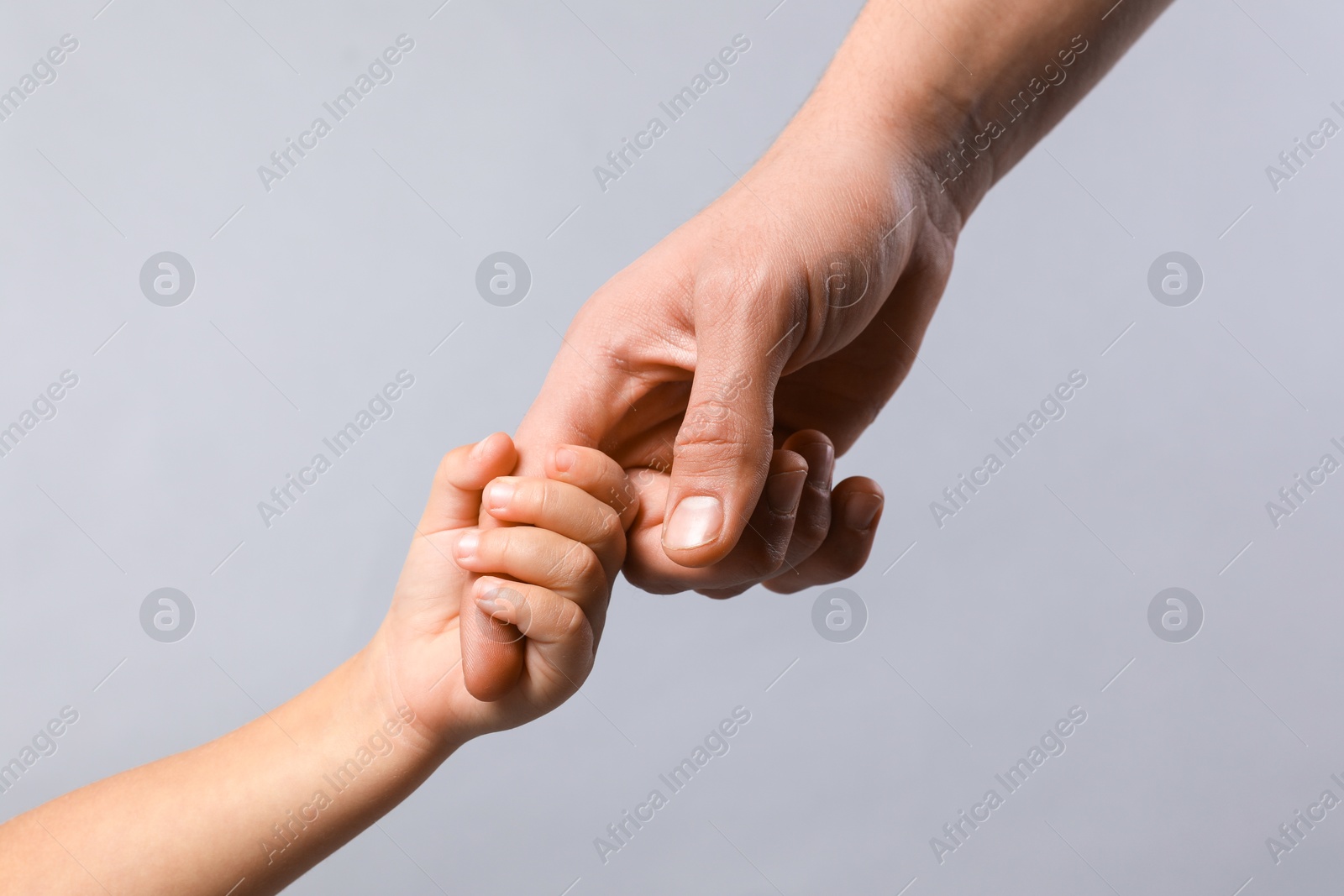 Photo of Father and child holding hands on grey background, closeup