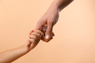 Photo of Father and child holding hands on beige background, closeup