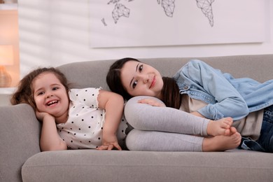 Photo of Cute little girl and her sister on sofa at home