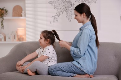 Photo of Teenage girl braiding her sister's hair on sofa at home