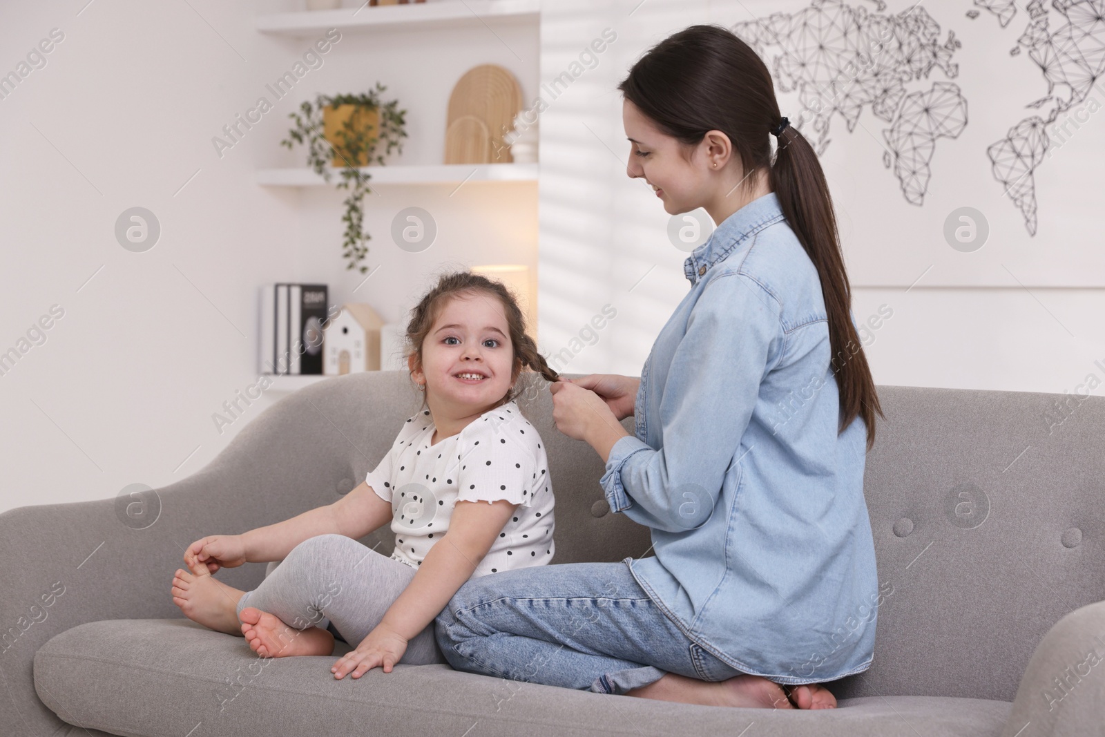 Photo of Teenage girl braiding her sister's hair on sofa at home