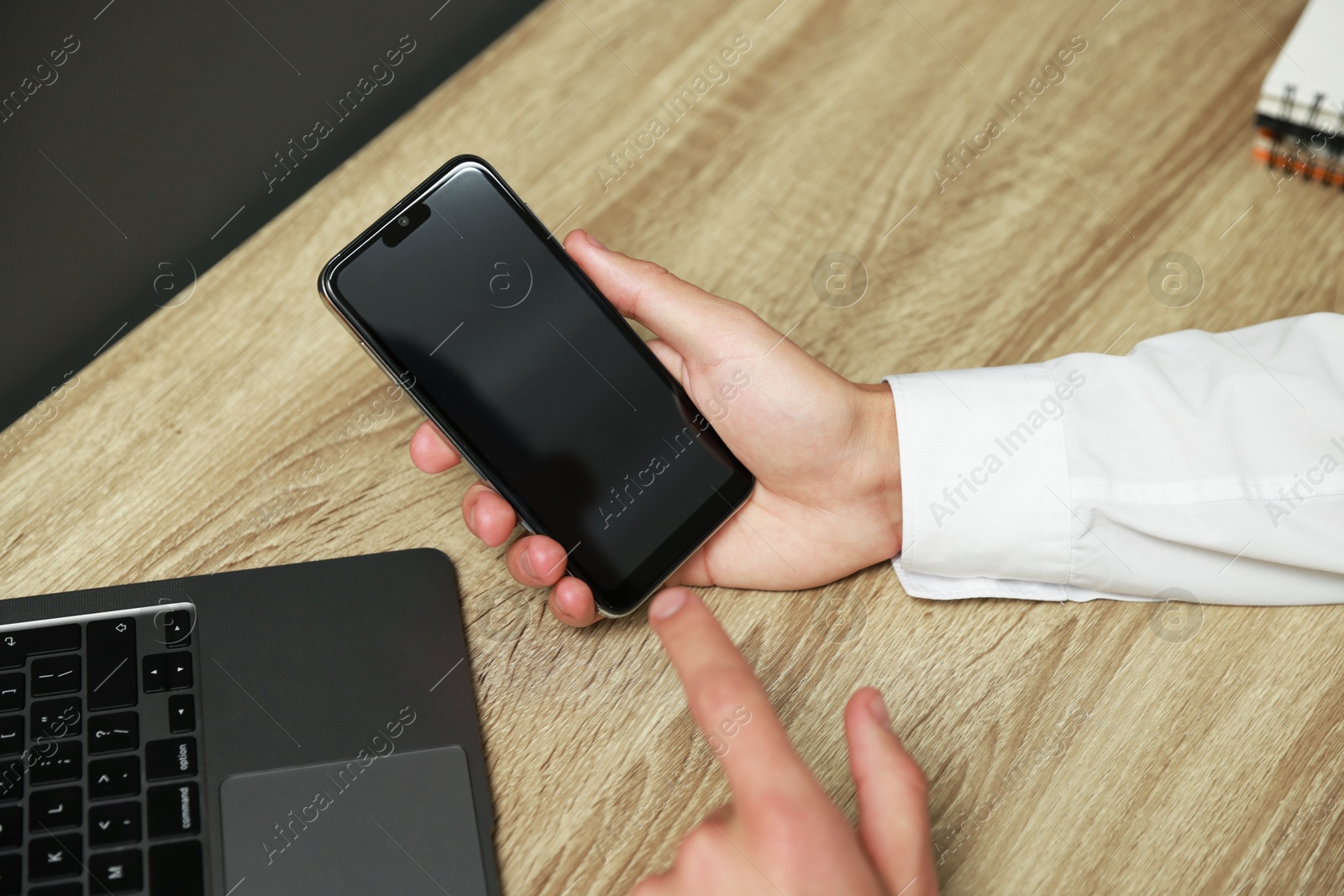 Photo of Man using smartphone with blank screen at wooden table, closeup