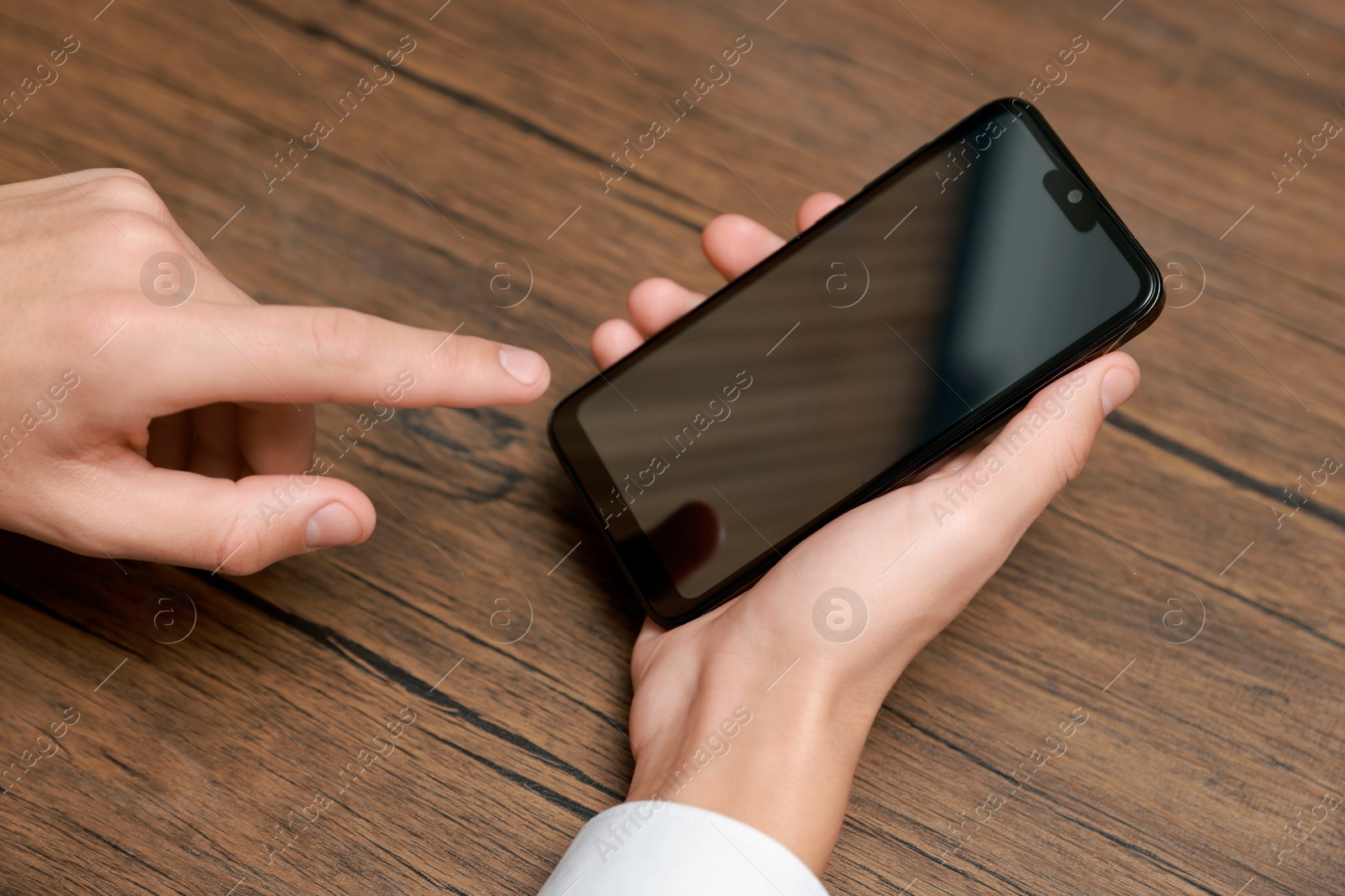 Photo of Man using smartphone with blank screen at wooden table, closeup