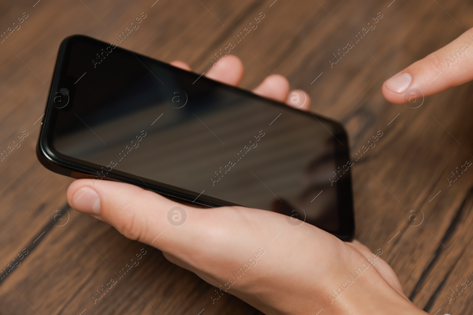 Photo of Man using smartphone with blank screen at wooden table, closeup