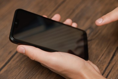 Photo of Man using smartphone with blank screen at wooden table, closeup