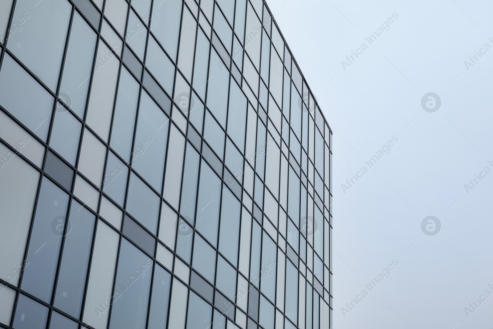 Photo of Modern building with many windows against blue sky, low angle view. Space for text