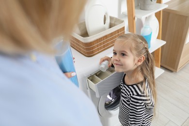 Photo of Little girl with detergent helping her mom doing laundry at home