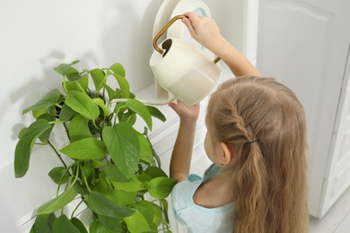 Photo of Little helper. Cute girl with watering houseplant at home