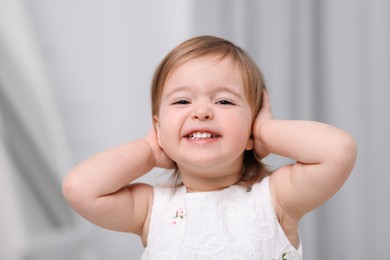 Photo of Cute little baby girl covering her ears on light grey background