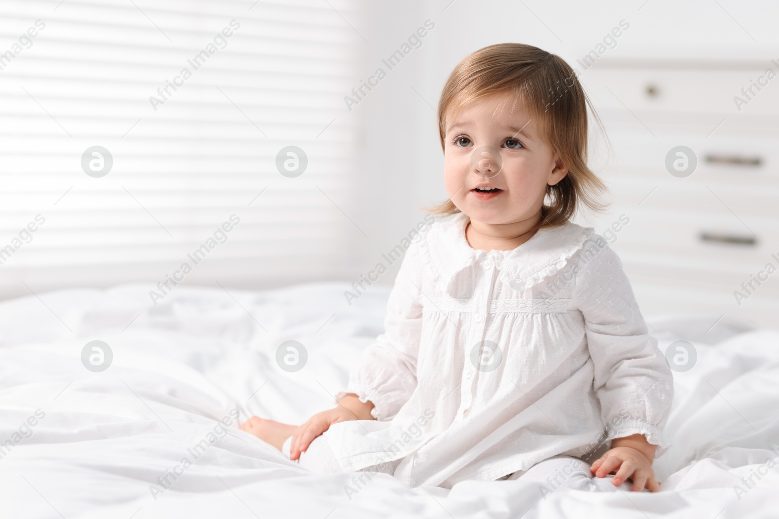 Photo of Cute little baby girl on bed at home. Space for text