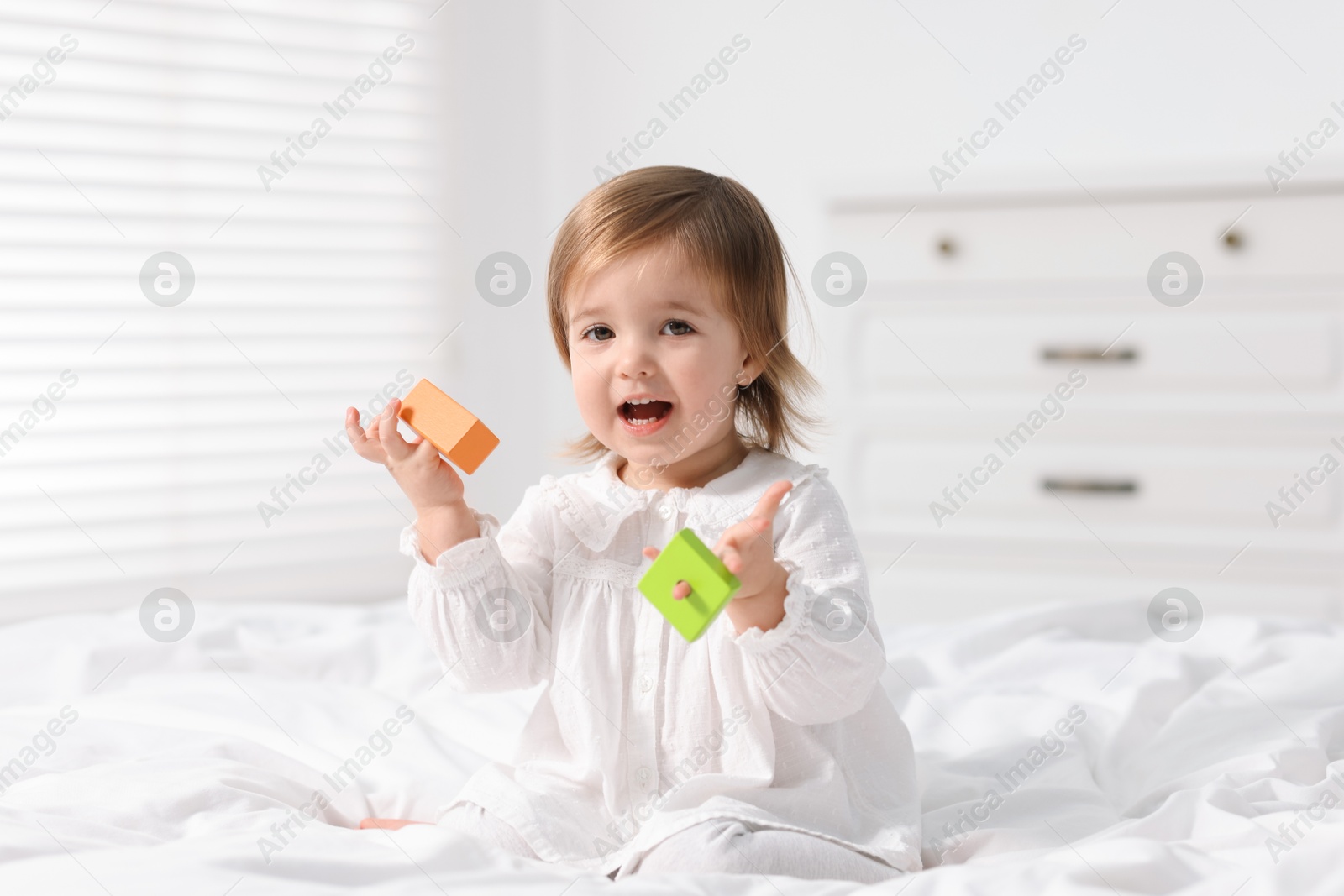 Photo of Cute little baby girl playing with toy on bed at home