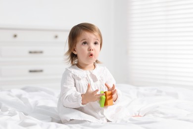 Photo of Cute little baby girl playing with toy on bed at home