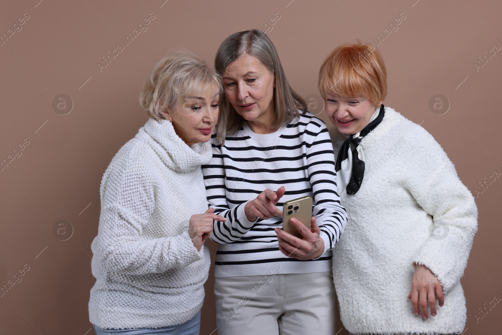 Photo of Senior woman showing something on smartphone to her friends against dark beige background