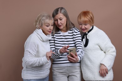 Photo of Senior woman showing something on smartphone to her friends against dark beige background