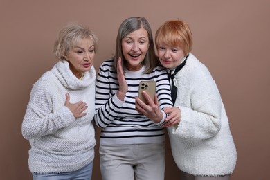 Photo of Senior woman showing something on smartphone to her friends against dark beige background