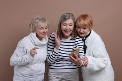 Photo of Senior woman showing something on smartphone to her friends against dark beige background