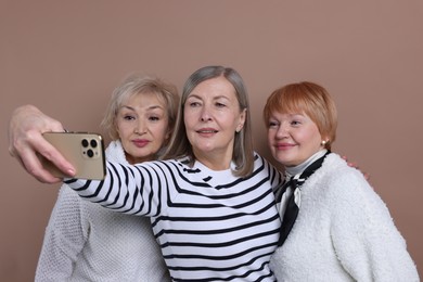 Friendship. Senior women taking selfie on dark beige background