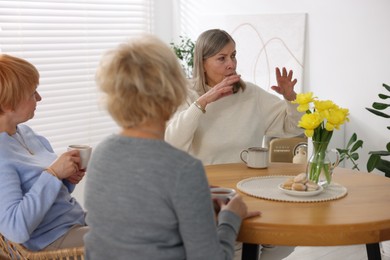 Friendship. Senior women enjoying hot drinks at table indoors