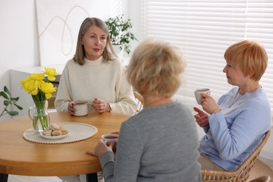 Friendship. Senior women enjoying hot drinks at table indoors