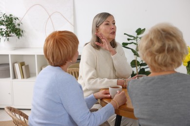 Photo of Friendship. Senior women enjoying hot drinks at table indoors