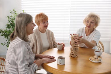 Photo of Friendship. Senior women building tower with wooden blocks at wooden table indoors