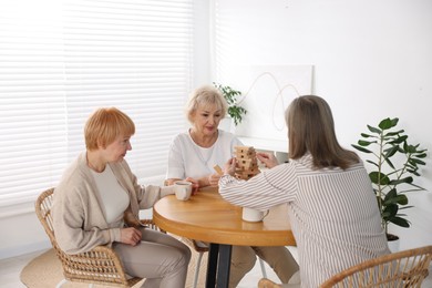 Photo of Friendship. Senior women building tower with wooden blocks at wooden table indoors