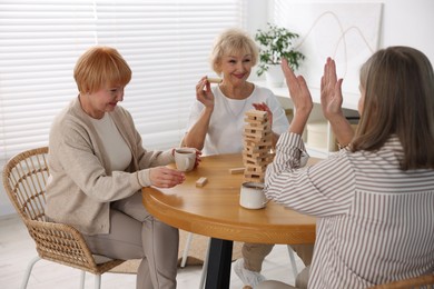 Photo of Friendship. Senior women building tower with wooden blocks at wooden table indoors