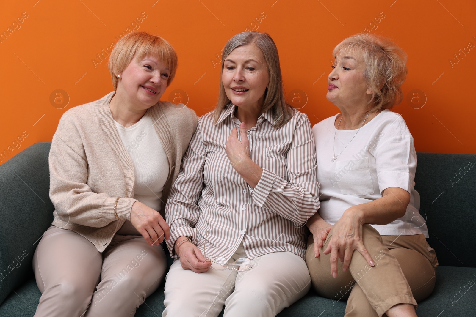 Photo of Friendship. Senior women on sofa near orange wall indoors