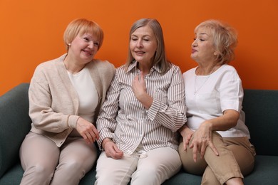 Photo of Friendship. Senior women on sofa near orange wall indoors