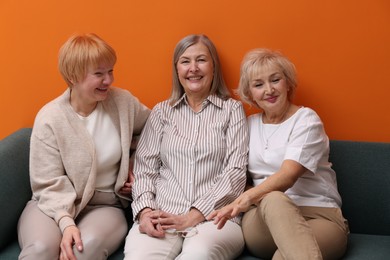 Friendship. Senior women on sofa near orange wall indoors