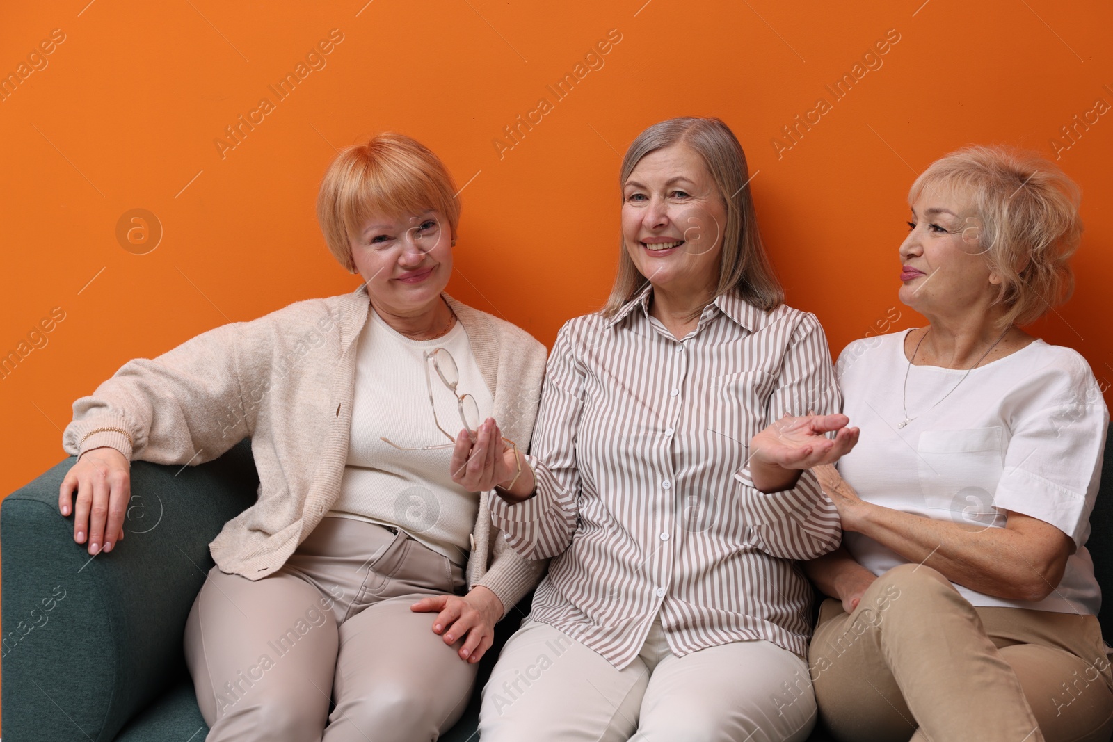 Photo of Friendship. Senior women on sofa near orange wall indoors