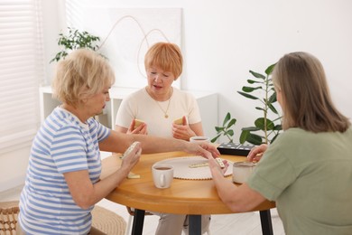 Photo of Friendship. Senior women playing dominoes at wooden table indoors