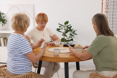 Photo of Friendship. Senior women playing dominoes at wooden table indoors