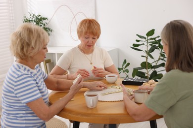 Photo of Friendship. Senior women playing dominoes at wooden table indoors