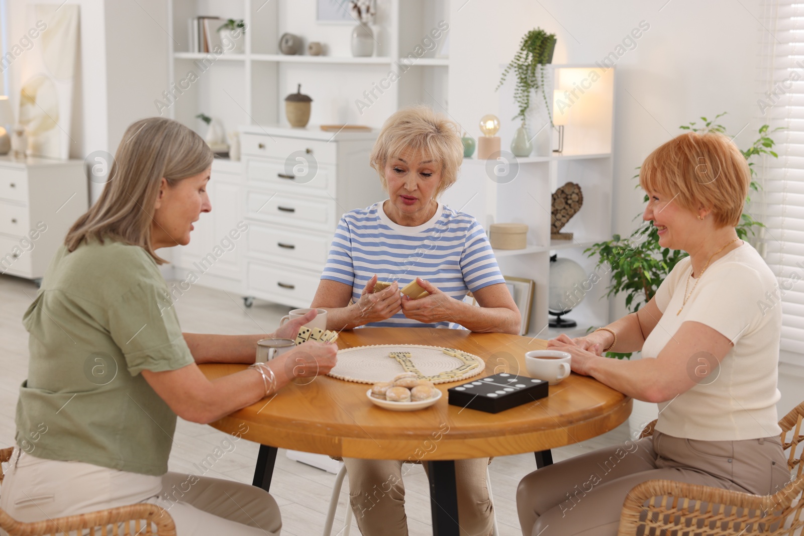 Photo of Friendship. Senior women playing dominoes at wooden table indoors