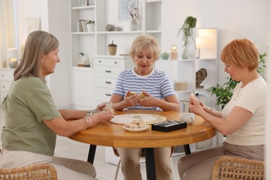 Photo of Friendship. Senior women playing dominoes at wooden table indoors