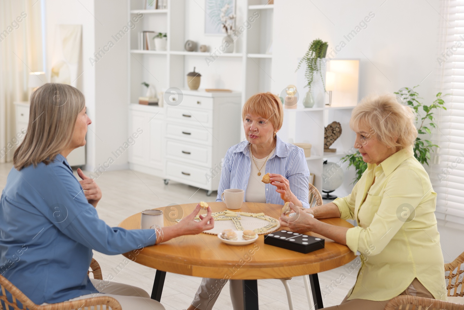 Photo of Friendship. Senior women enjoying hot drinks and cookies at table indoors