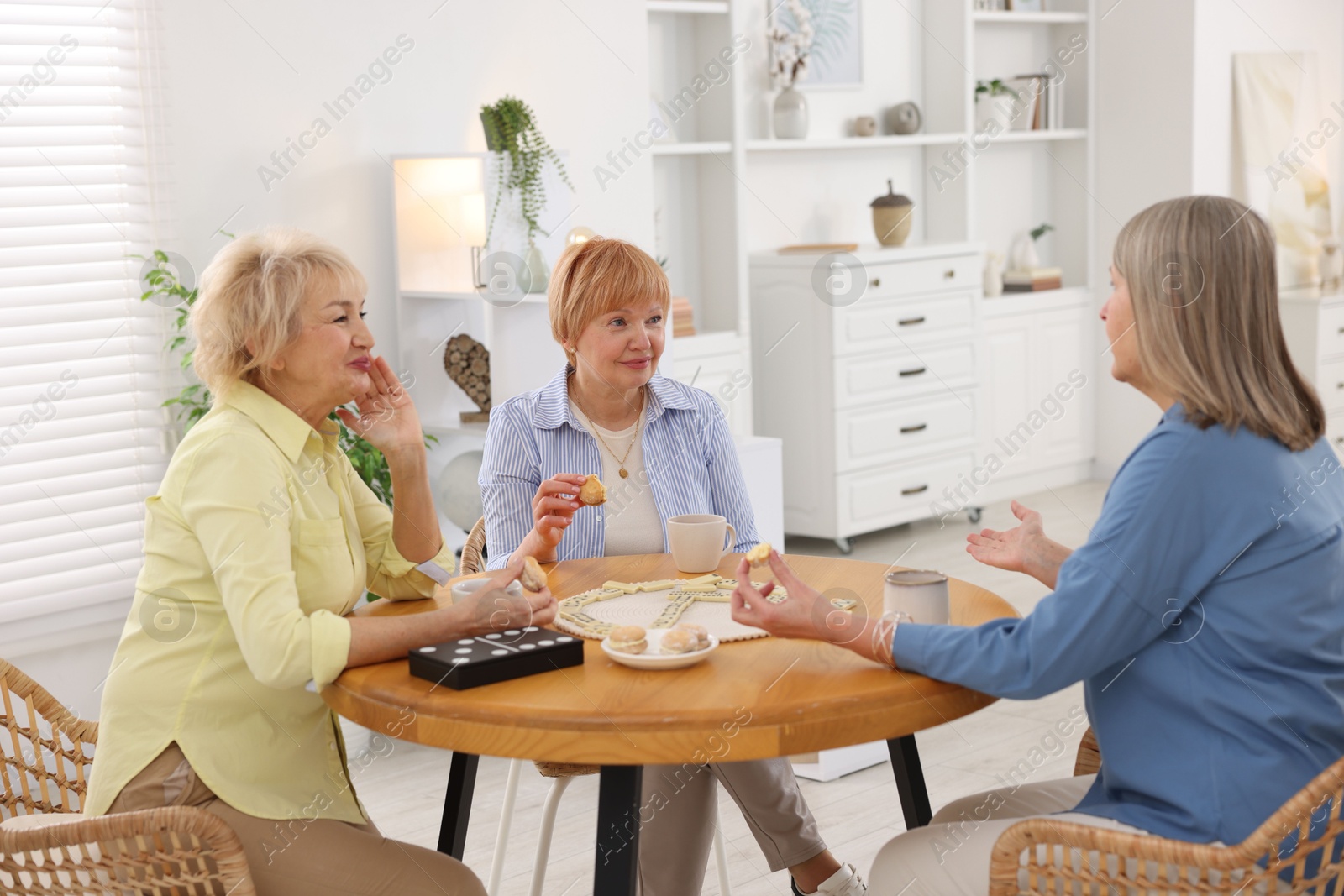 Photo of Friendship. Senior women enjoying hot drinks and cookies at table indoors