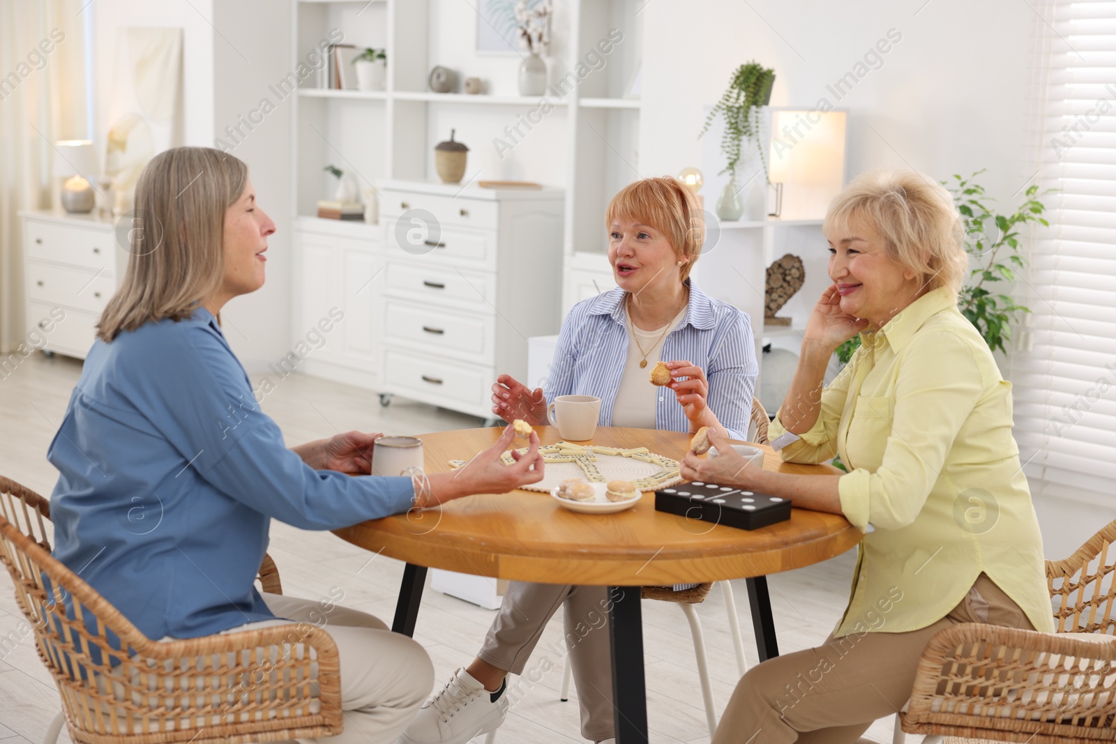 Photo of Friendship. Senior women enjoying hot drinks and cookies at table indoors