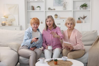 Photo of Friendship. Senior women watching tv on sofa at home