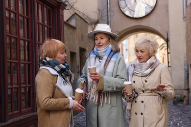 Friendship. Senior women enjoying hot drinks on city street