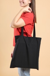 Photo of Woman with blank black shopper bag on color background, closeup. Mockup for design