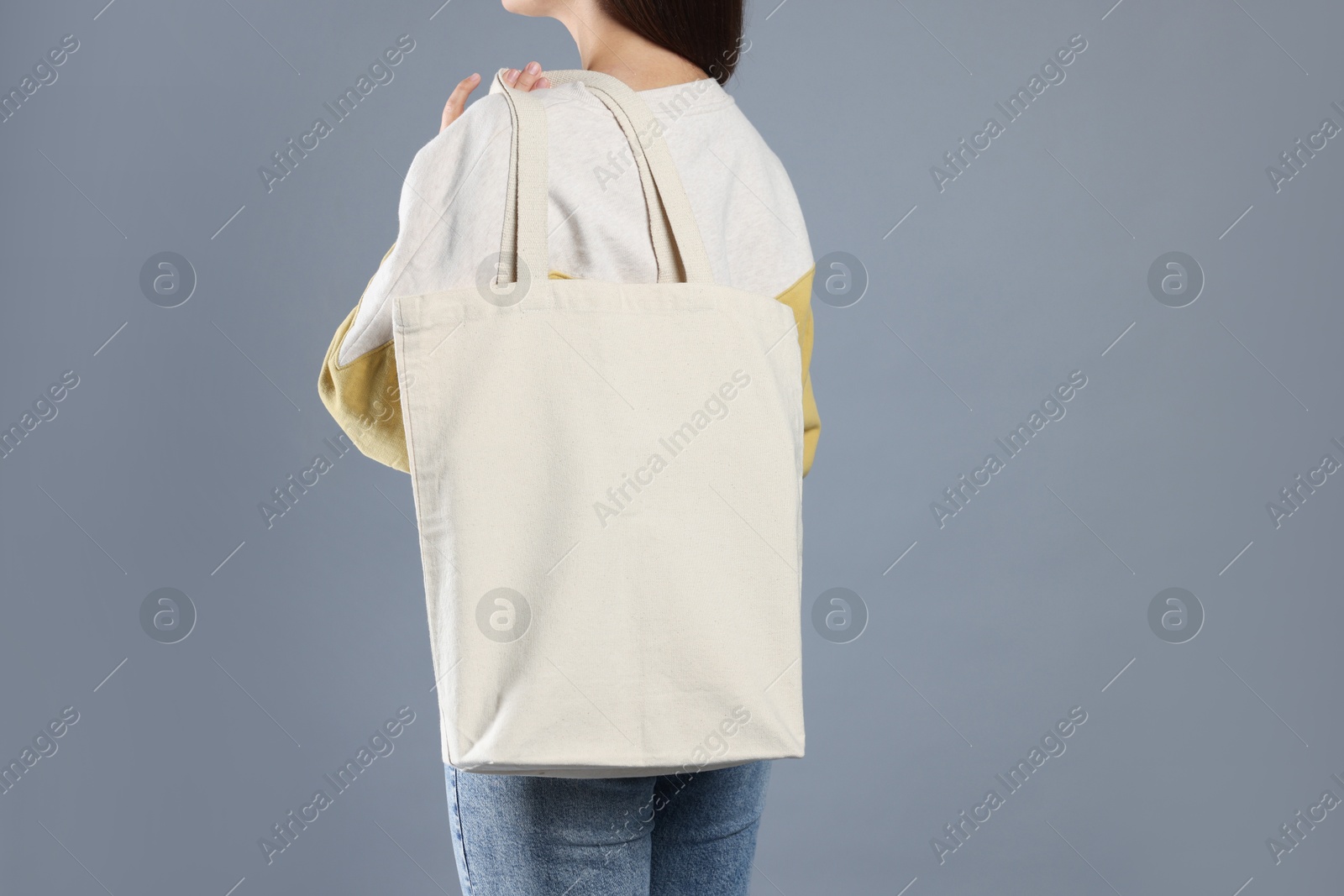 Photo of Woman with blank shopper bag on grey background, back view. Mockup for design