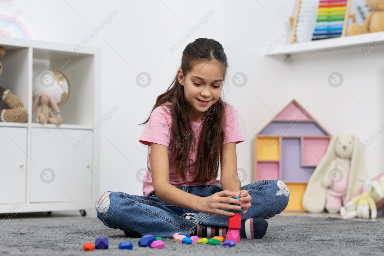 Photo of Girl playing with balancing stones on floor indoors