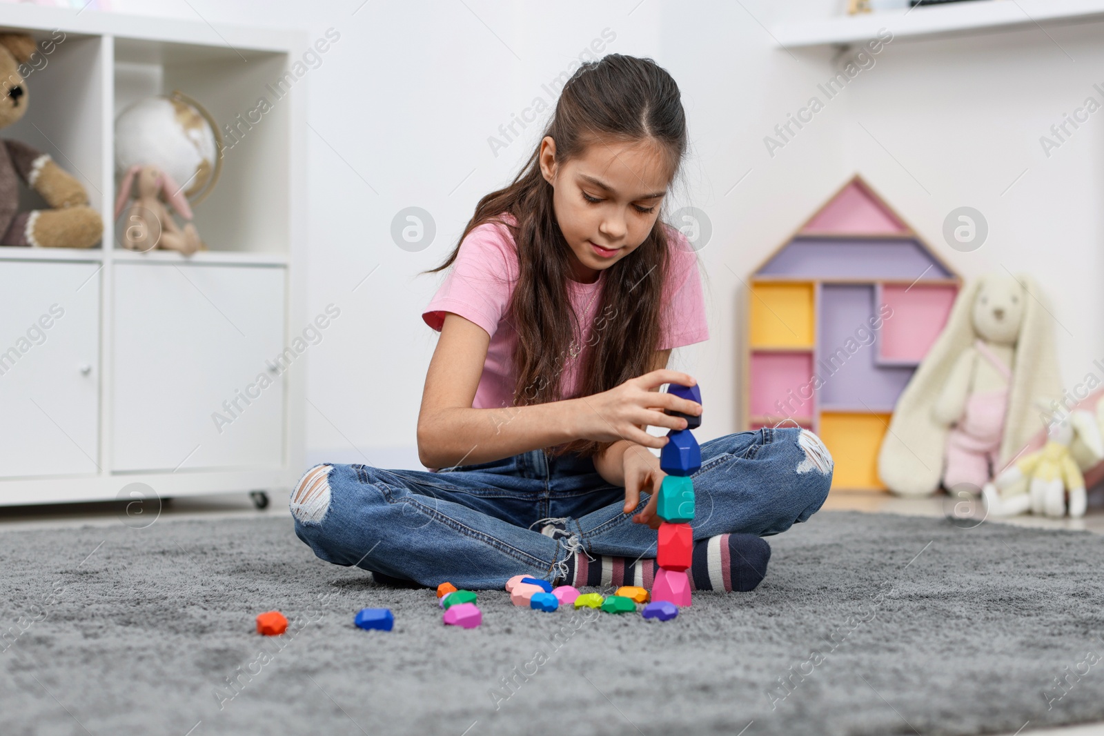 Photo of Girl playing with balancing stones on floor indoors