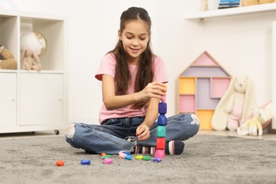 Photo of Girl playing with balancing stones on floor indoors