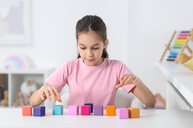 Girl with colorful cubes at table indoors